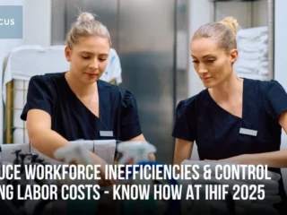 Two female healthcare workers in dark scrubs work at a station, with a UNIFOCUS logo in the top-left and a banner about reducing workforce inefficiencies for IHF 2025.