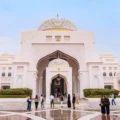 White marble mosque courtyard with grand arched entry, domed roof, and visitors exploring the plaza.