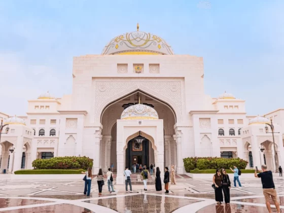 White marble mosque courtyard with grand arched entry, domed roof, and visitors exploring the plaza.