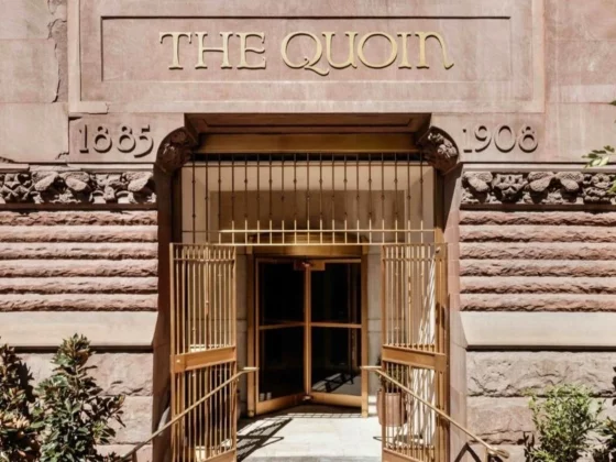 Entrance to The Quoin building with ornate stone facade and open gold gates; the sign reads THE QUOIN above the doorway.
