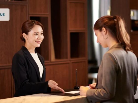 Receptionist in a blazer greets a guest at a marble front desk in a lobby; UNIFOCUS logo visible on the top-left corner.