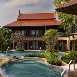 Luxury resort courtyard with a curved pool, tropical plants, and a Thai-style building with a red roof.
