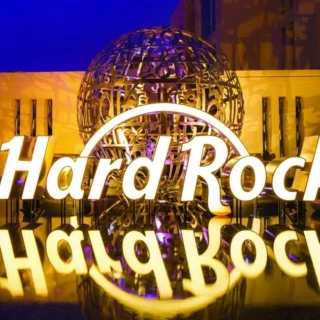 Illuminated Hard Rock sign with reflection on a glossy surface at night, blue sky and decorative globe behind it