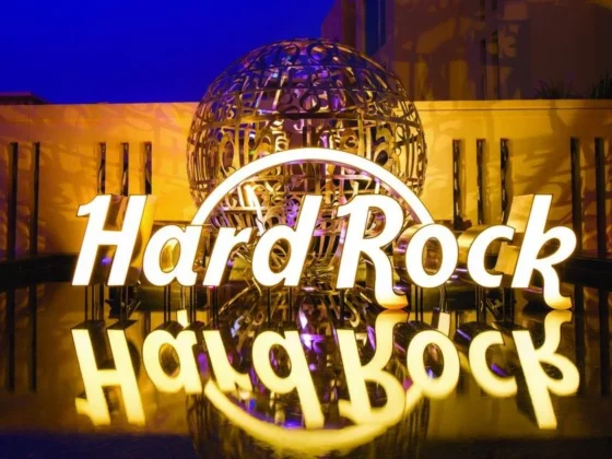 Illuminated Hard Rock sign with reflection on a glossy surface at night, blue sky and decorative globe behind it