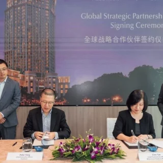 Formal signing ceremony at a conference table with two people signing documents, flanked by two standing officials; a banner reads 'Global Strategic Partnership Signing Ceremony' in English and Chinese.