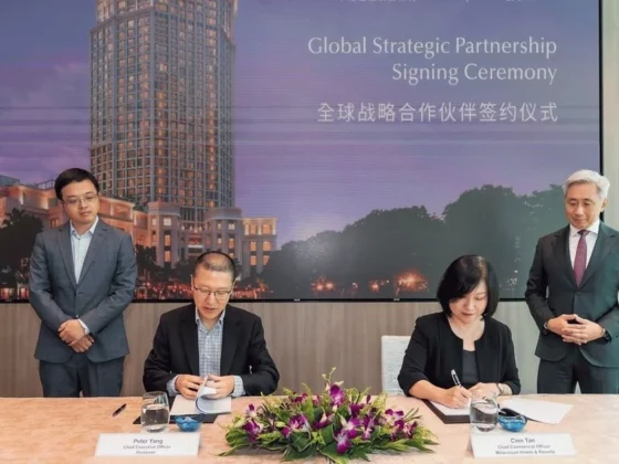 Formal signing ceremony at a conference table with two people signing documents, flanked by two standing officials; a banner reads 'Global Strategic Partnership Signing Ceremony' in English and Chinese.