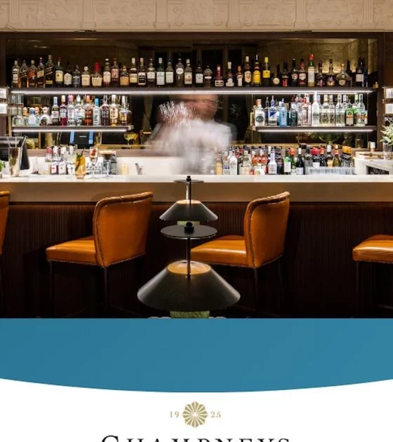 Bar interior with a white counter, backlit bottles on glass shelves, and four orange leather stools along the counter