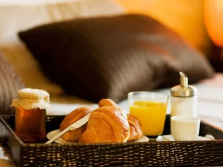 Bedside breakfast tray on a bed with croissants, orange juice, and small condiments.