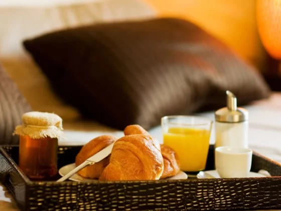 Bedside breakfast tray on a bed with croissants, orange juice, and small condiments.