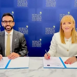 Two professionals sign documents at a signing table, with a blue World Travel & Tourism Council backdrop behind them.