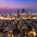 Aerial view of a city at twilight with illuminated buildings and a pink-purple sky at dusk.”,