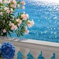 Seaside balcony with pink oleander flowers and blue hydrangeas overlooking sparkling blue water.