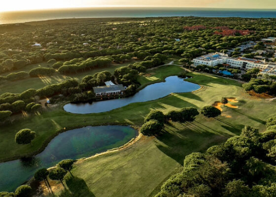 Aerial view of a golf course with ponds, greens, and a clubhouse nestled among trees at sunset.