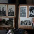 Open photo album with black-and-white family photos on brown pages; hands hold the edges of the scrapbook.