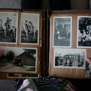 Open photo album with black-and-white family photos on brown pages; hands hold the edges of the scrapbook.