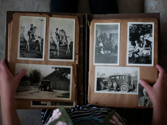 Open photo album with black-and-white family photos on brown pages; hands hold the edges of the scrapbook.