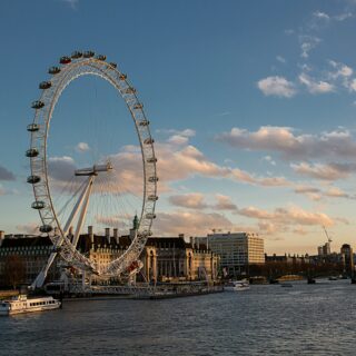 London Eye ferris wheel along the River Thames at sunset with boats nearby and a city skyline in the background