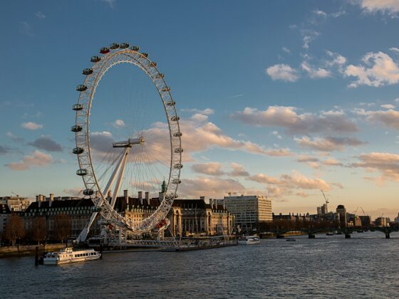 London Eye ferris wheel along the River Thames at sunset with boats nearby and a city skyline in the background