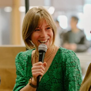 Smiling woman in a green lace top speaks into a handheld microphone during a conversation.