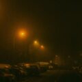 Night street scene at night with orange streetlights casting a hazy glow over parked cars and a foggy atmosphere