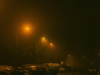 Night street scene at night with orange streetlights casting a hazy glow over parked cars and a foggy atmosphere
