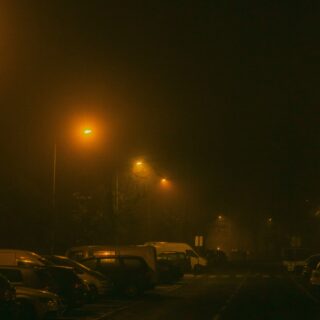 Night street scene at night with orange streetlights casting a hazy glow over parked cars and a foggy atmosphere