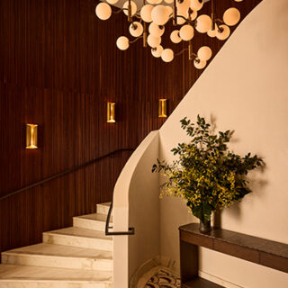 Interior stairwell with marble steps, curved white wall, dark wood panels, a modern globe chandelier, and a potted plant on a console.