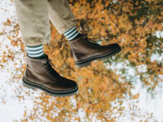 Person wearing brown lace-up boots stepping through fallen autumn leaves with green-and-white striped socks visible above the boots
