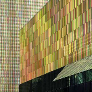 Colorful building facade with vertical rainbow-hued metal panels and a small black-framed window.