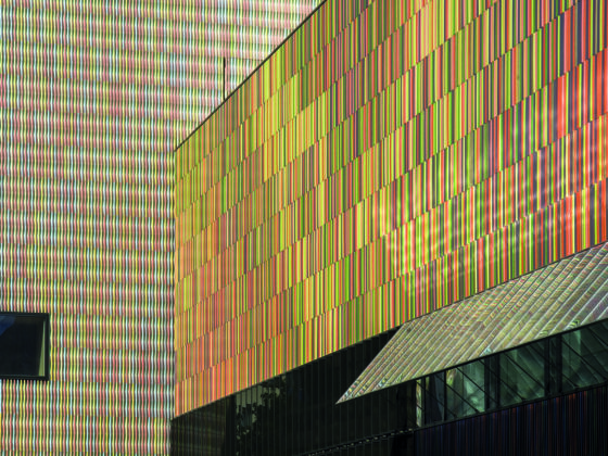 Colorful building facade with vertical rainbow-hued metal panels and a small black-framed window.