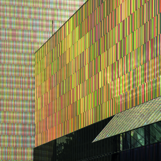 Colorful building facade with vertical rainbow-hued metal panels and a small black-framed window.