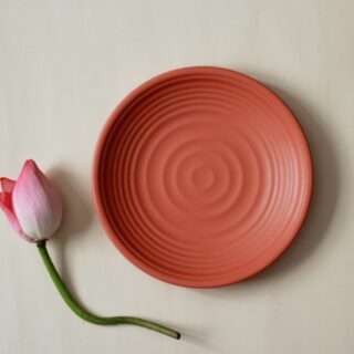 Close-up of a pink ceramic plate with a pink rosebud and green stem placed along its edge on a pale background, flat lay.