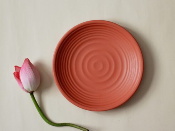 Close-up of a pink ceramic plate with a pink rosebud and green stem placed along its edge on a pale background, flat lay.