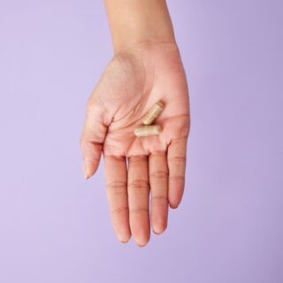 Hand holding three beige capsule pills against a purple background.
