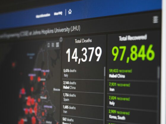 Blurred dashboard showing country-by-country COVID-19 stats with a 'Total Deaths' column and large white numbers.