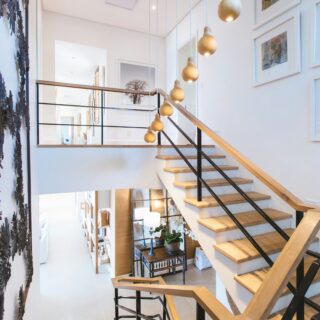 Modern open staircase in a bright white foyer with wooden steps, black metal railing, and gold pendant lights hanging along the wall.