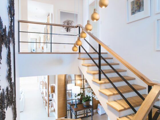 Modern open staircase in a bright white foyer with wooden steps, black metal railing, and gold pendant lights hanging along the wall.