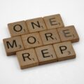 Wooden Scrabble tiles spell the words 'ONE MORE' arranged diagonally on a white background.