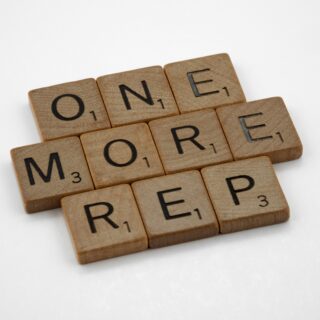 Wooden Scrabble tiles spell the words 'ONE MORE' arranged diagonally on a white background.