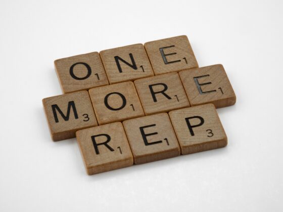 Wooden Scrabble tiles spell the words 'ONE MORE' arranged diagonally on a white background.