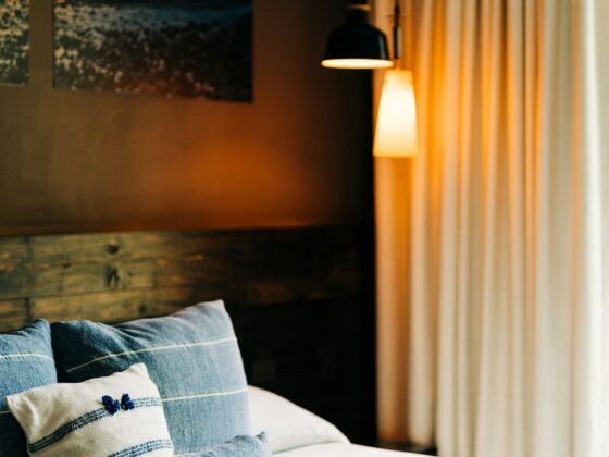 Bed with blue-striped pillows on white linens, a wall photo, and warm lamps beside beige curtains for a cozy bedroom scene.