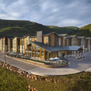 Modern mountain resort hotel with multiple amber-brown wings and a glass entrance, set on a hillside with outdoor seating.