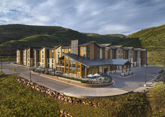 Modern mountain resort hotel with multiple amber-brown wings and a glass entrance, set on a hillside with outdoor seating.