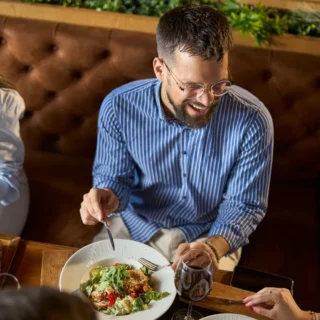 Three friends sit at a booth, smiling and sharing a meal; a salad plate and a fried appetizer platter with dipping sauce are on the table.