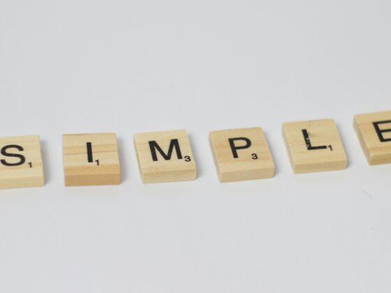 Wooden Scrabble-style tiles spell the word 'SIMPLE' in a row on a light background.