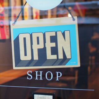 Open sign hanging in a storefront window with a blurred shop interior behind it.