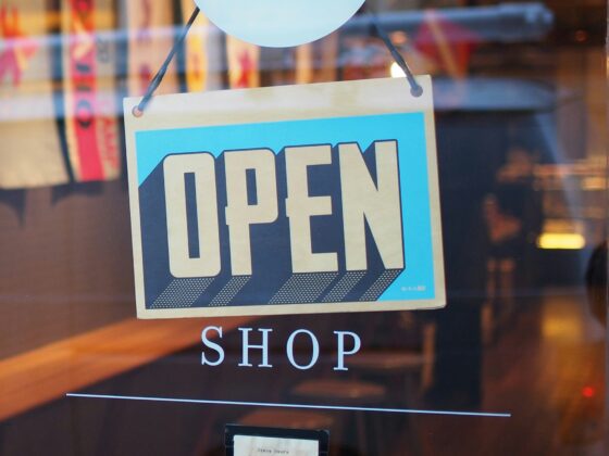 Open sign hanging in a storefront window with a blurred shop interior behind it.