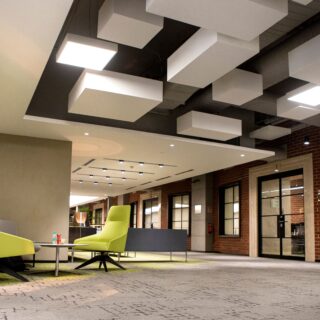 Open lobby seating area with lime-green chairs and white geometric ceiling blocks in a modern office interior at dusk/low light.