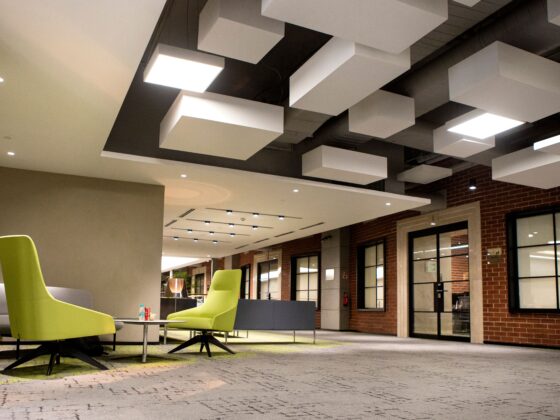 Open lobby seating area with lime-green chairs and white geometric ceiling blocks in a modern office interior at dusk/low light.