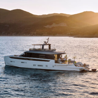 Luxury catamaran-style yacht on calm sea at sunset, with hills in the background and people dining on the deck.